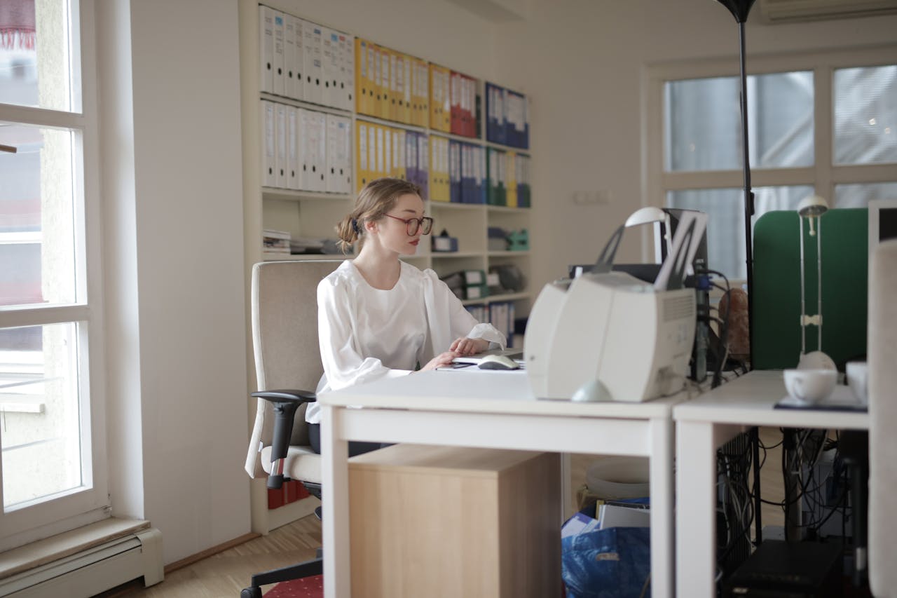 Home Focused woman working in a modern office filled with files and equipment.
